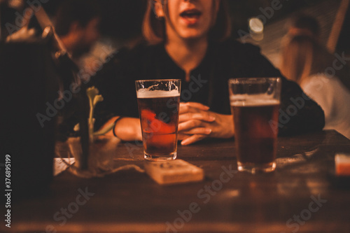 Giovane ragazza seduta al tavolo di un locale serale all'aperto con davanti due bicchieri di birra fresca