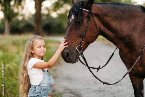 Friendship of a child with a horse. A little girl is affectionately stroking her horse. Walking girls with a horse in the park in autumn.