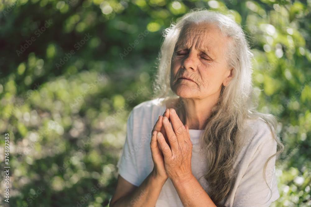 The gray-haired grandmother is praying in outdoors. Faith, spirituality and religion concept. The gray-haired grandmother is praying in outdoors. Faith, spirituality and religion concept.