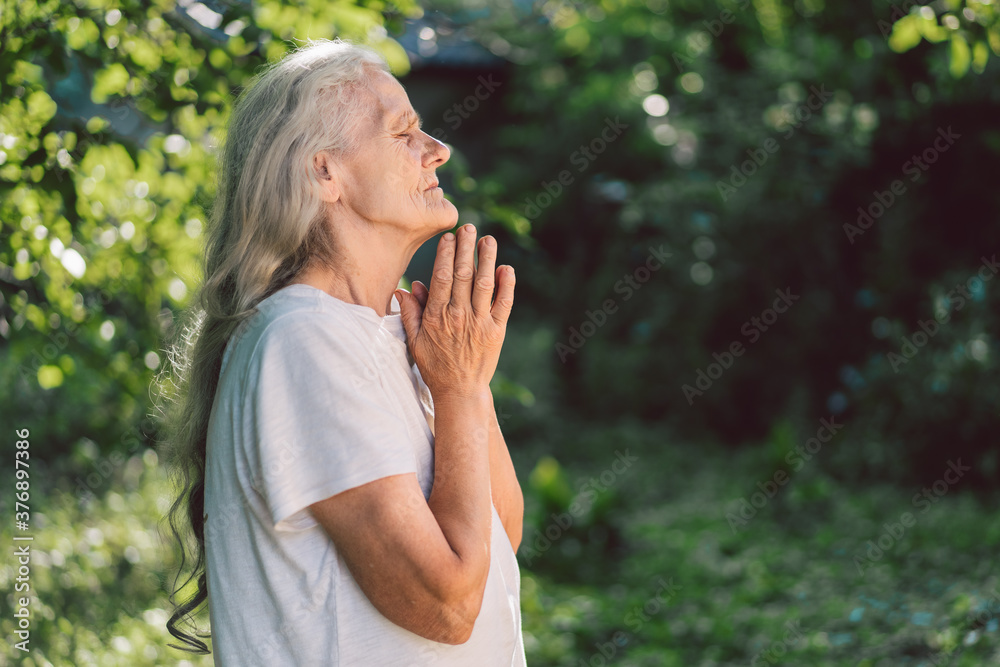The gray-haired grandmother is praying in outdoors. Faith, spirituality and religion concept. The gray-haired grandmother is praying in outdoors. Faith, spirituality and religion concept.