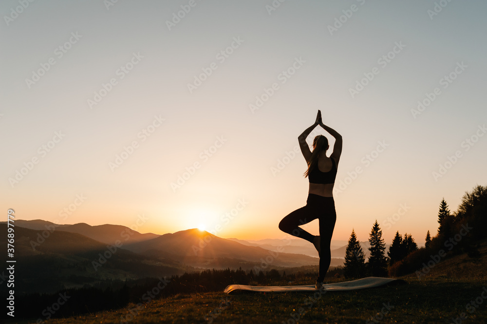 Meditation. Silhouette woman balanced, practicing meditate and zen energy yoga in mountains. Healthy lifestyle concept. Girl doing fitness exercise sport outdoors. Morning sunrise. Back view.