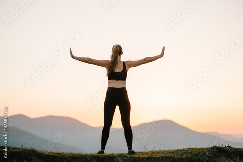 Woman balanced, practicing meditation, zen energy yoga in mountains. Healthy lifestyle concept. Young girl doing fitness exercise sport outdoors. Morning sunrise. Relax in nature. Back view.