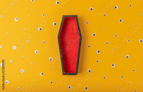 Halloween yellow background with an open red-black coffin in the center, around a scattering of plastic eyes of different sizes. A place for your product. photo