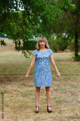 A young blonde woman in a blue dress stands in a city park.