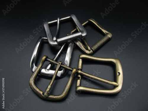 Lots of metal belt buckles on a black background. Copper, brass.