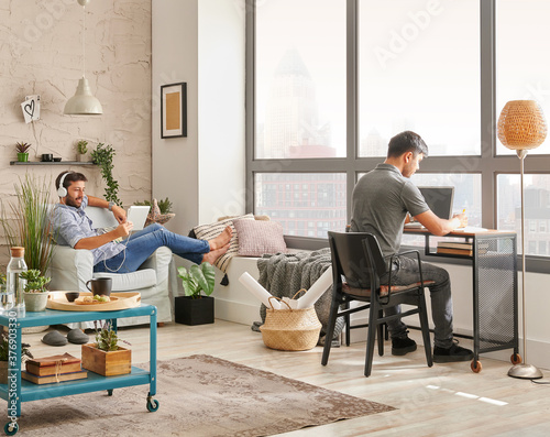 Two man friends in the room and working together. Listening to the music and modern decoration style.