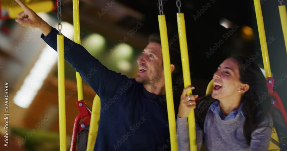 A happy carefree smiling couple in love is having fun to make selfie or video call to friends or family while riding chain swing carousel together in amusement park at night. A happy carefree smiling couple in love is having fun to make selfie or video call to friends or family while riding chain swing carousel together in amusement park at night.
