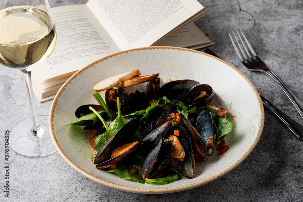 Mussels salad with fresh mini spinach on a grey stone table with a glass of white wine