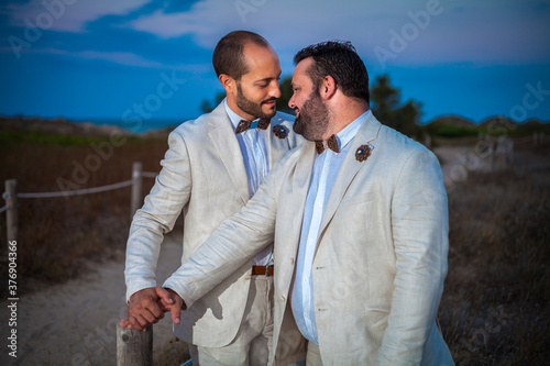 Just married gay wedding couple in white suits look at each other in love