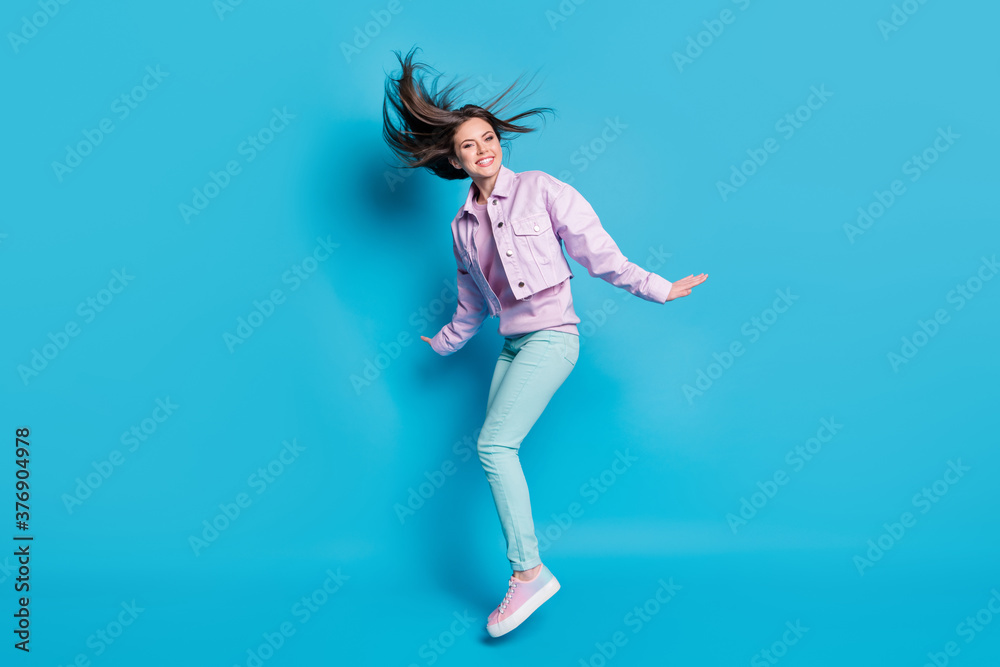 Full length profile photo of funny lady jumping high up rejoicing sunny day good weather hairdo flight wear casual denim violet jacket sweater pants shoes isolated blue color background