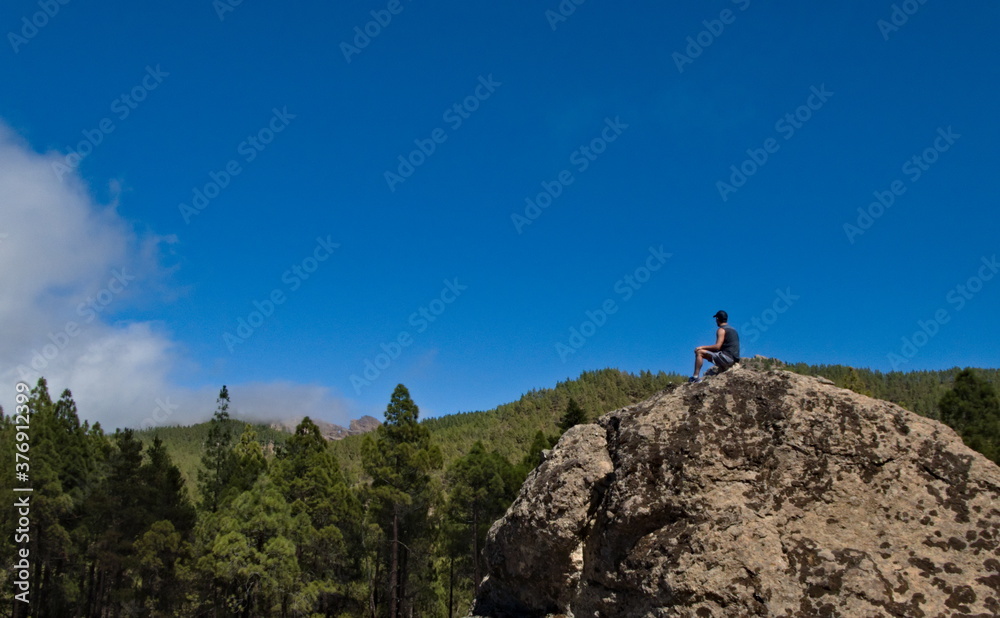 A lonely man sitting on a rock and contemplating a mountain landscape