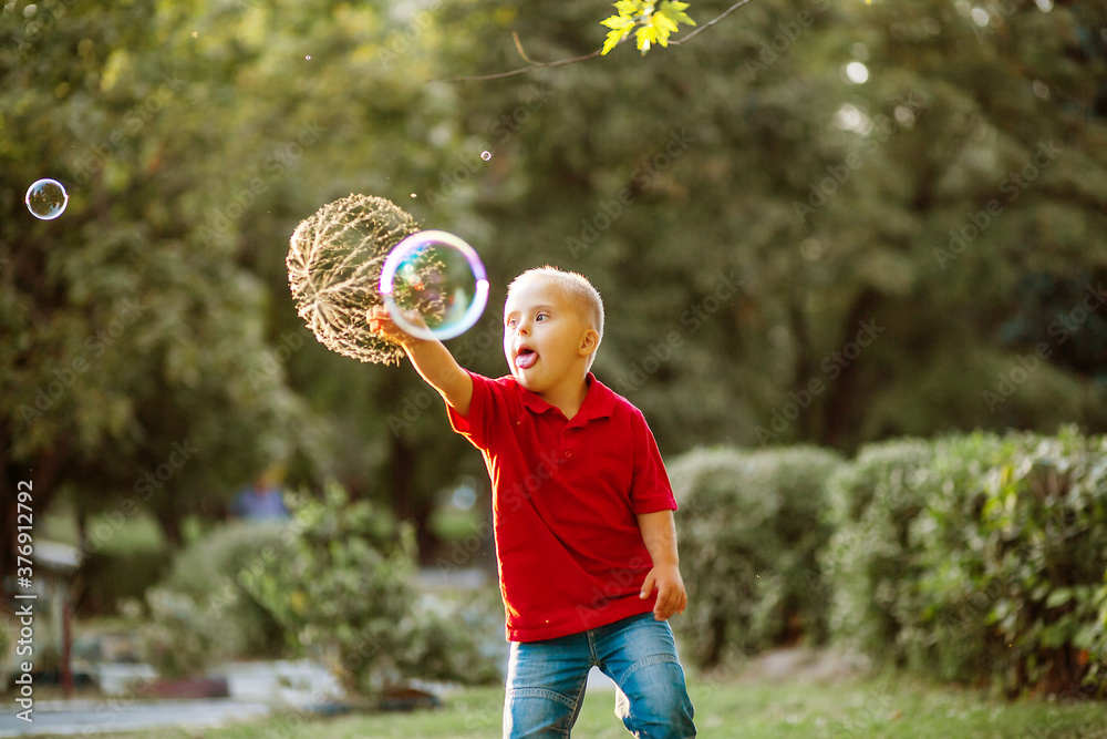 Little cute boy with Down Syndrome plays with huge soap bubbles in the