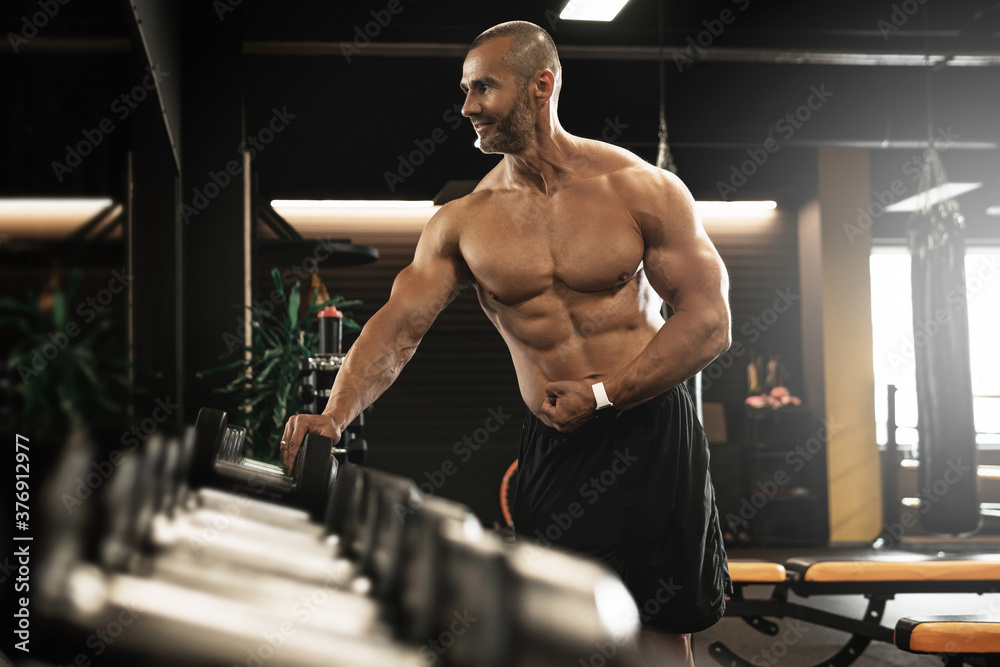 Muscular bodybuilder in a free weights zone in the gym Muscular bodybuilder in a free weights zone in the gym