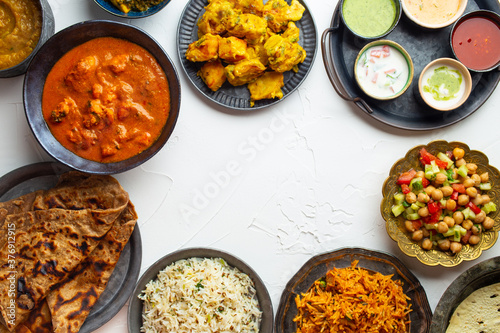 Variety of Indian food, different dishes and snacks on white rustic background. Pilaf, butter chicken curry, rice, palak paneer, chicken tikka, dal soup, naan bread, assortment of chutney. Top view.