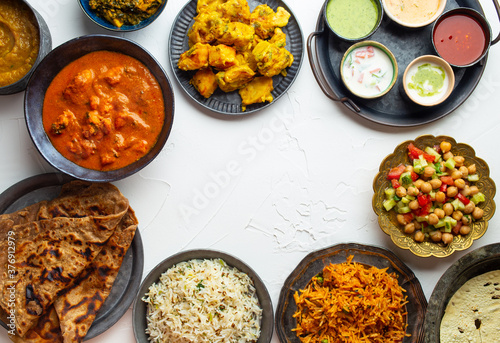 Variety of Indian food  different dishes and snacks on white rustic background. Pilaf  butter chicken curry  rice  palak paneer  chicken tikka  dal soup  naan bread  assortment of chutney. Top view.