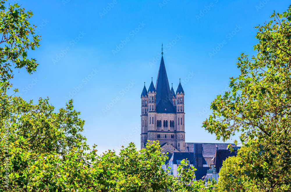 Tower with spire of Great Saint Martin Roman Catholic Church Romanesque architecture style building with green trees foreground, blue clear sky, North Rhine-Westphalia, Germany