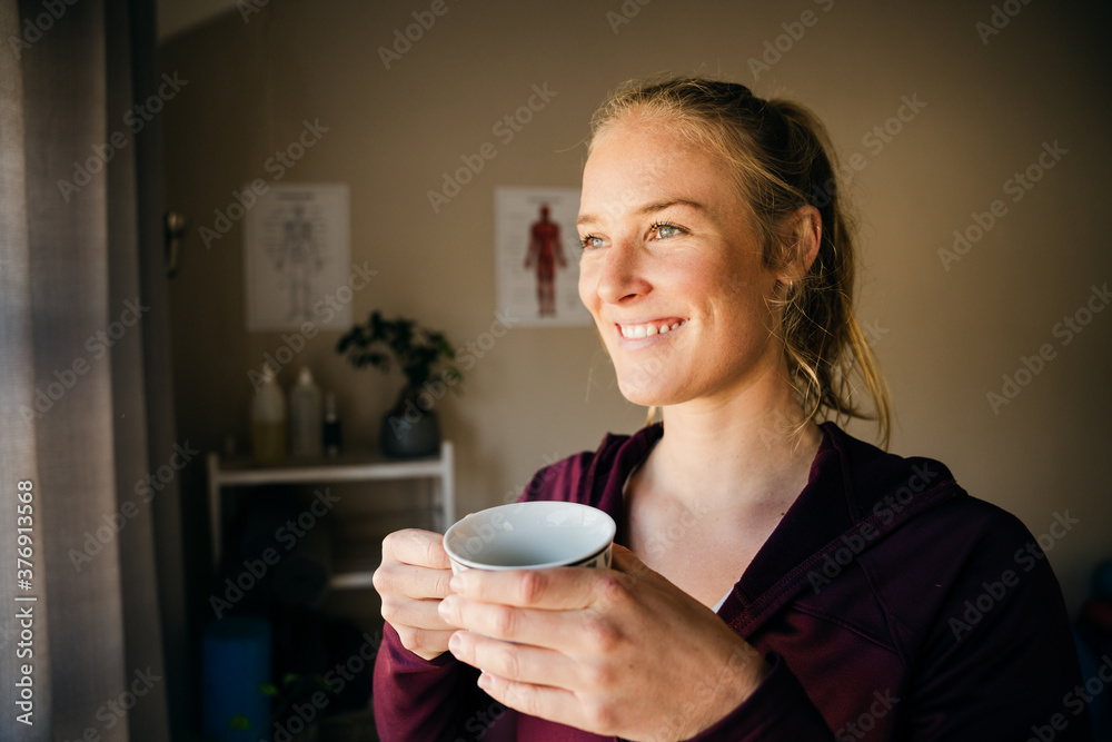 Beautiful caucasian woman standing in physio studio holding cup of hot coffee Beautiful caucasian woman standing in physio studio holding cup of hot coffee