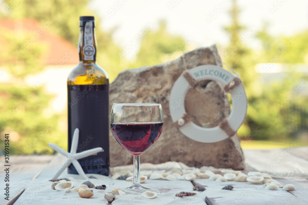 Bottle of wine and wine glass on wooden table with sand and rock.