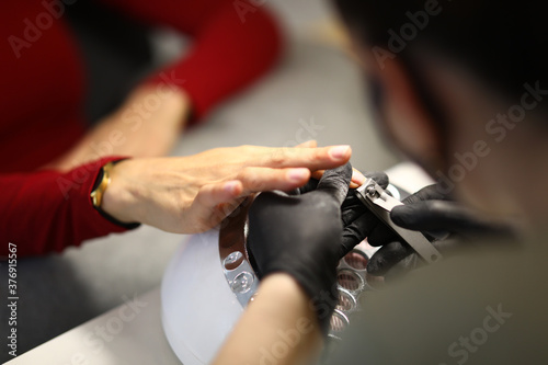 Gloved manicurist uses nippers to process nails in salon. Manicure tools concept.