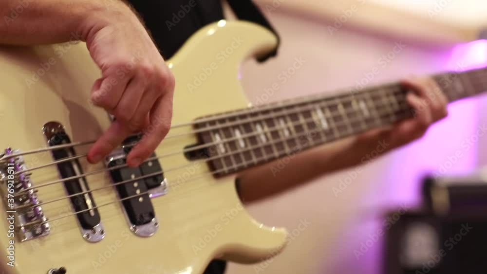 Closeup of male bassist hands playing on electric bass guitar touching strings on rehearsal