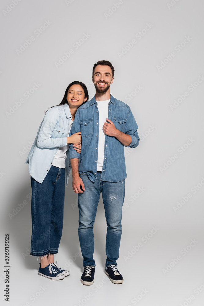 full length view of stylish asian woman leaning on bearded boyfriend in denim clothes on grey full length view of stylish asian woman leaning on bearded boyfriend in denim clothes on grey