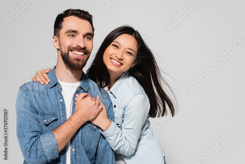 young asian woman looking at camera while holding hands with boyfriend isolated on grey