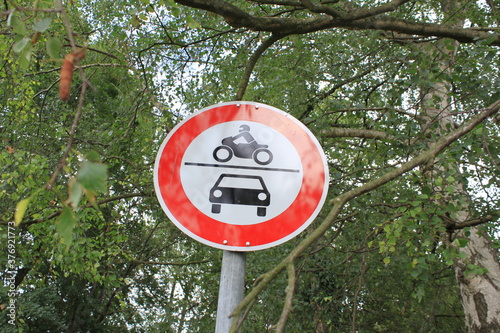 Straßenschild mit Auto und Motorrad Verbot. Im Hintergrund stehen Bäume.