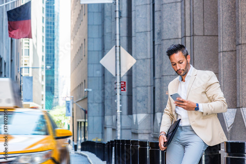 Obraz na płótnie Young European Businessman traveling, working in New York, with beard, little gray hair, wearing beige blazer, gray pants, holding briefcase, sitting on old street, looking down, texting on cell phone w salonie