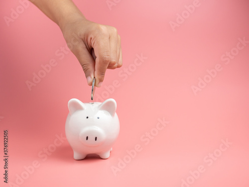 White piggy Bank on a pink background and human hand putting coin in piggy bank. copyspace for design.