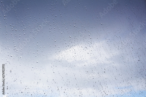 Raindrops on the window pane. Blue cloudy sky behind.