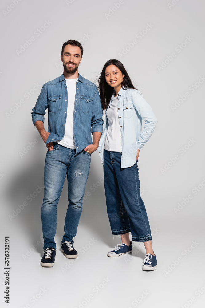 full length view of stylish interracial couple in jeans and denim shirts looking at camera on white full length view of stylish interracial couple in jeans and denim shirts looking at camera on white
