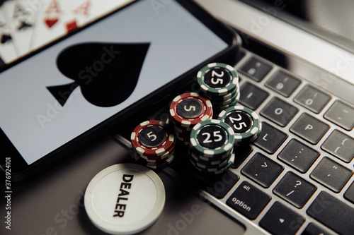 Online poker casino theme. Gambling chips, smartphone and playing cards on laptop keyboard.