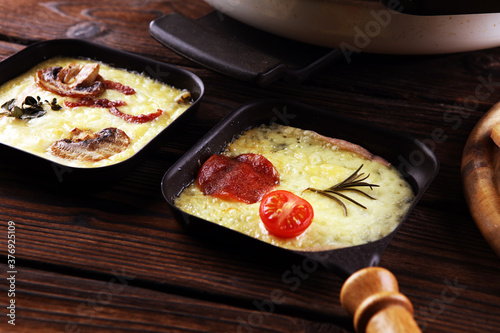 Delicious traditional Swiss melted raclette cheese served in individual skillets with salami and bacon photo