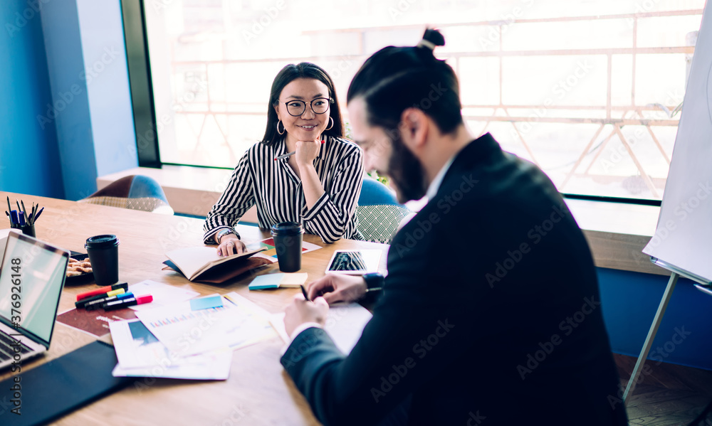 Fototapeta premium Smiling elegant ethnic adult businesswoman in workplace during meeting with coworker in office