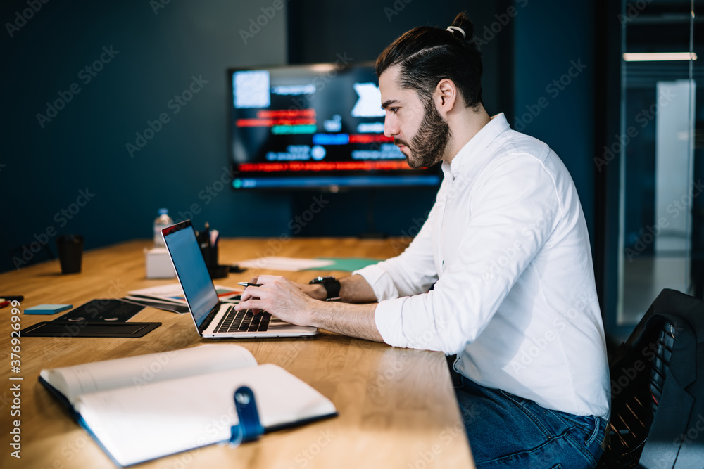 Fototapeta premium Serious manager using laptop and sitting at table in office