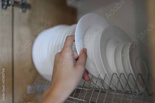 Woman's hand pulls clean white dishes out of kitchen cabinet. Household helpers services concept photo