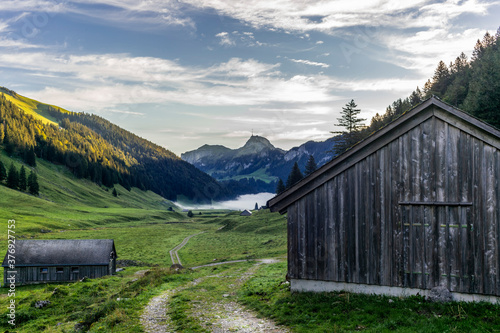 The path leading to the Sämtisersee lake covered in fog early in the morning amond old wooden stables and cottages in Appenzell photo