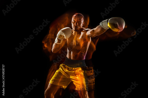Fireball. Professional boxer training isolated on black studio background in mixed light. Man in gloves practicing in kicking and punching. Healthy lifestyle, sport, workout, motion and action concept