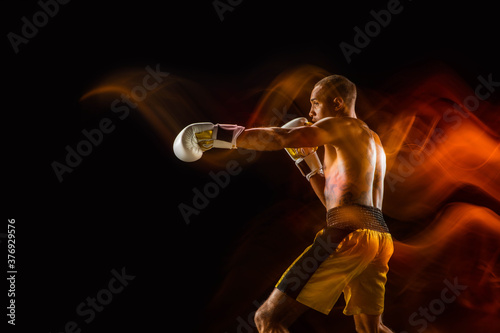 Fireball. Professional boxer training isolated on black studio background in mixed light. Man in gloves practicing in kicking and punching. Healthy lifestyle, sport, workout, motion and action concept © master1305