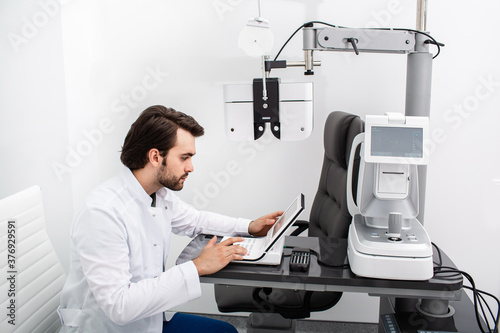 Experienced optometrist sitting at his workplace in a modern ophthalmology clinic. Vision test and vision diagnostics
