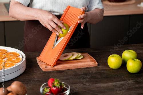 Close-up of unrecognizable woman using mandoline slicer for cutting apple while preparing fruits for dehydration at home photo