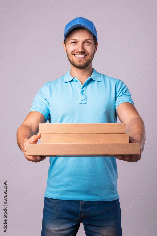 Young delivery man is holding boxes with a delicious pizza Young delivery man is holding boxes with a delicious pizza