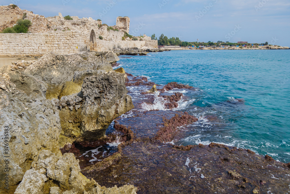 Remains of stone dam, washing by sea waves. Building on background is ancient castle Corycus in Kizkalesi, Turkey. It's in tentative UNESCO World Heritage List