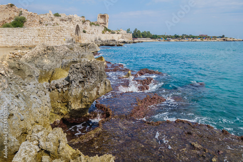 Remains of stone dam, washing by sea waves. Building on background is ancient castle Corycus in Kizkalesi, Turkey. It's in tentative UNESCO World Heritage List