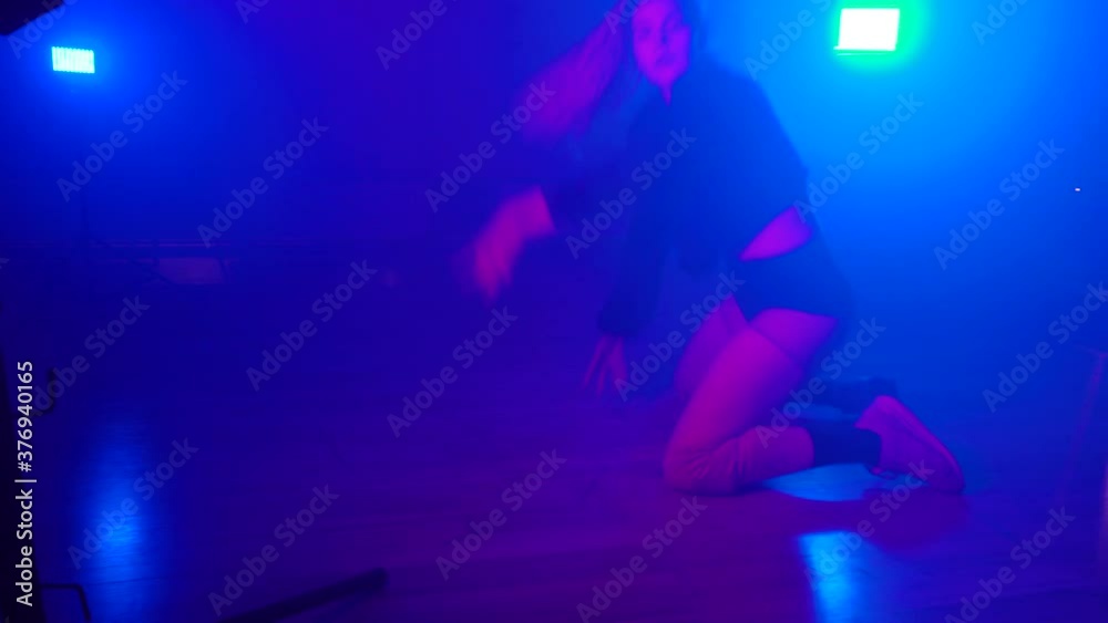 Sexy woman wearing hoody and transparent shorts twerking on floor in dark foggy dance studio, blue flashlight on background. Female dancer shaking her booty. Concept of choreography Sexy woman wearing hoody and transparent shorts twerking on floor in dark foggy dance studio, blue flashlight on background. Female dancer shaking her booty. Concept of choreography