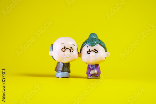 Miniature people, elderly people standing on yellow background using as family and insurance concept
