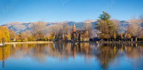 Panoramic view of the Puigcerda lake in the middle of the autumn at sunset where the trees with golden leaves are reflected in the lake. Puigcerda, Catalonia, Spain