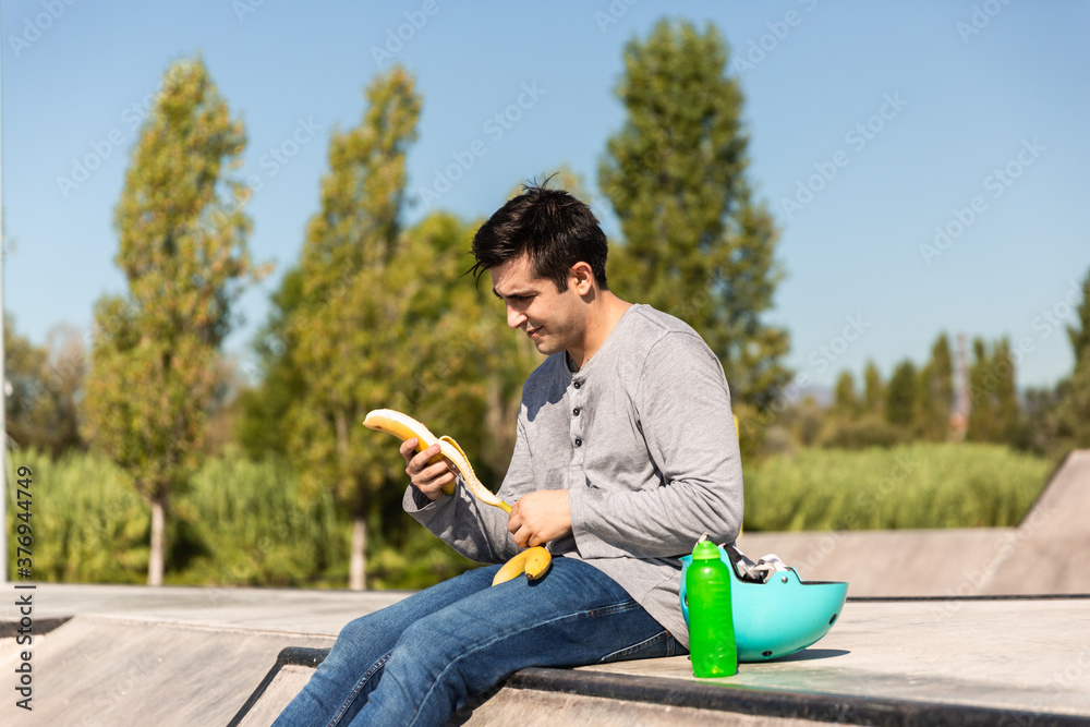 Obraz premium roller boy eating a banana sitting in a skate park