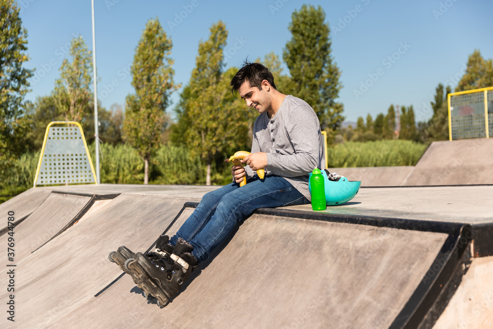 roller boy eating a banana sitting in a skate park