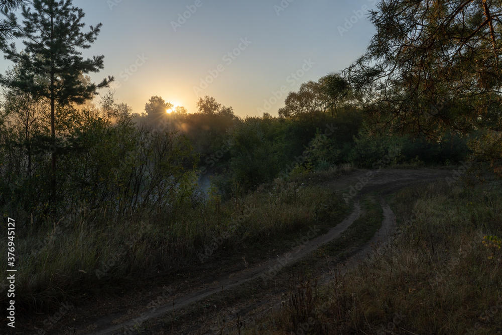 Autumn time. Dawn over the river in a misty, brooding haze. Beautiful view of the forest and river, covered with fog in the early morning. The sun's rays of light.